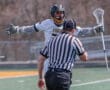 Lacrosse player celebrating a play while engaging with the referee on the field during a sunny day game.