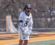 Lacrosse player in white jersey preparing for action on the field, displaying teamwork and athleticism during practice.