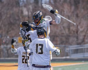 Lacrosse team celebrates a goal, showcasing teamwork and excitement on a sunny field during a spirited match.