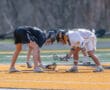 Two lacrosse players prepare for a faceoff on a bright, orange turf field during a game.