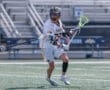 Lacrosse player in white uniform maneuvering on the field, showcasing athleticism and skill during a game.
