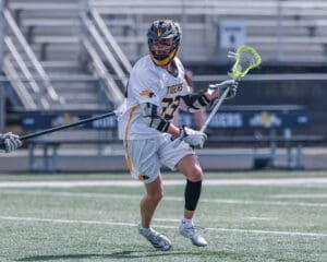 Lacrosse player in white uniform maneuvering on the field, showcasing athleticism and skill during a game.