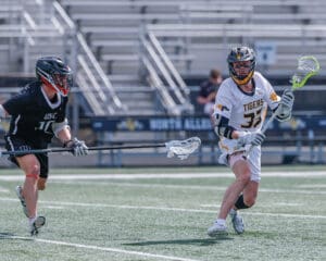 Two lacrosse players competing on the field, with one in a black uniform and the other in white.