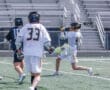 High school lacrosse players in action, one throwing the ball while two opponents defend on the field.
