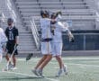 Two lacrosse players celebrate a goal with a joyful hug during a match, showcasing team spirit and sportsmanship.
