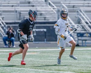 Two young lacrosse players compete on the field, showcasing athleticism during an outdoor game.