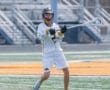 Lacrosse player in white jersey practicing on the field, preparing to pass the ball with a focused expression.