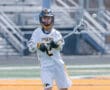 Young lacrosse player in team uniform preparing to pass the ball during a game on a sunny day.