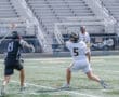 Lacrosse players in action on the field; one player passes while another defends. Competitive sports moment captured.