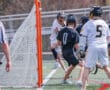Lacrosse players in action, one shooting at the goal while others defend during a competitive match.