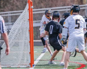 Lacrosse players in action, one shooting at the goal while others defend during a competitive match.