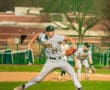 High school baseball player wearing a Tigers uniform throws a pitch on the mound during a sunny day game.