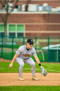 A young baseball player in a Tigers uniform prepares to field a ball on the infield during a game.