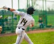 Young baseball player in a gray uniform swings a bat on the field during practice, showcasing athleticism and focus.