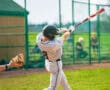 A baseball player in gray uniform swings a bat during a game, while the pitcher prepares to throw.