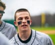 Baseball player in gray jersey speaks passionately to teammates, showcasing determination and team spirit on the field.