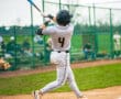 Young baseball player in action, swinging a bat during a game on a sunny field.