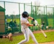 A young baseball player swings his bat, making contact with the ball during a sunny game on the diamond.