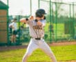 Baseball player in Tigers uniform prepares to swing bat on sunny field during a game, with spectators in the background.