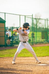 Baseball player in Tigers uniform prepares to swing bat on sunny field during a game, with spectators in the background.