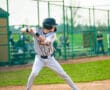 Young baseball player in a gray uniform prepares to swing at the pitch on a sunny day at the field.
