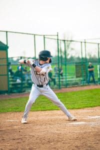 Young baseball player in a gray uniform prepares to swing at the pitch on a sunny day at the field.