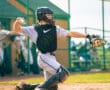 Young baseball catcher in uniform prepares to throw a ball from behind home plate during a game on a sunny day.