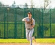 Baseball player in uniform throwing a ball on a sunny field, showcasing athletic skills and teamwork.