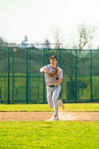 Baseball player in uniform throwing a ball on a sunny field, showcasing athletic skills and teamwork.