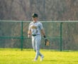 A baseball player in a gray uniform walks on a green field, wearing sunglasses and a glove, ready for the game.