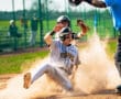 A baseball player slides into home plate, kicking up dust, as the umpire calls the play during an exciting game.