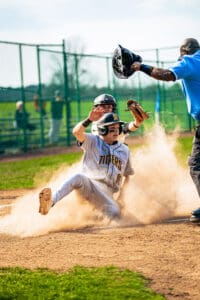 A baseball player slides into home plate, kicking up dust, as the umpire calls the play during an exciting game.