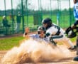 A baseball player slides into home plate while a catcher prepares to tag him in a dynamic outdoor game scene.