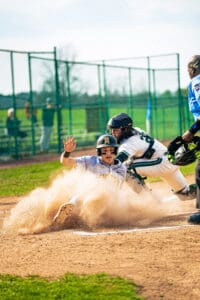 A baseball player slides into home plate while a catcher prepares to tag him in a dynamic outdoor game scene.
