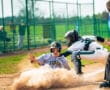 A young baseball player slides into home plate as the catcher prepares for the play, dust swirling around them.