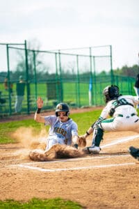 Baseball player slides into home plate while catcher prepares to tag him during an exciting game on a sunny day.
