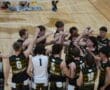 High school volleyball team in black and gold jerseys huddling together, celebrating teamwork and camaraderie on the court.