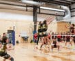 Boys volleyball match in action, players jumping at the net while spectators watch enthusiastically.