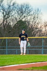 Young baseball player in a Tigers uniform stands on the field, holding a glove and looking focused during practice.