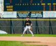 Baseball player in action on the field with scoreboard displaying game stats and team name Tigers.