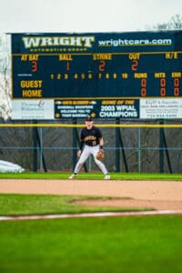 Baseball player in action on the field with scoreboard displaying game stats and team name Tigers.