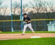 Young baseball player in a black jersey prepares to field a ball on a diamond, with a blurred background of a field.