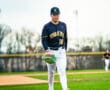 Baseball player wearing a Tigers jersey and cap walks confidently on the field, ready to pitch.