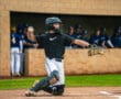 Baseball catcher in action, preparing to throw a pitch during a game, with players in the dugout in the background.