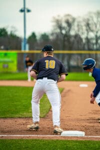 A baseball player wearing jersey number 10 stands at first base, ready for the next play in a game.