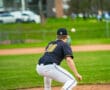 A baseball player crouches at first base, ready to catch a ball during a game on a grassy field.