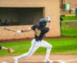 A baseball player swings a bat during a game, preparing to hit a pitch on a field with green grass.