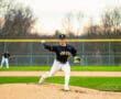 High school baseball pitcher on the mound windup, ready to throw in a vibrant green field setting.