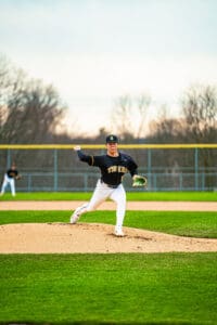 High school baseball pitcher on the mound windup, ready to throw in a vibrant green field setting.