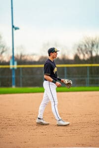 Baseball player in a black jersey and white pants walking on the field, focused and ready for the game.